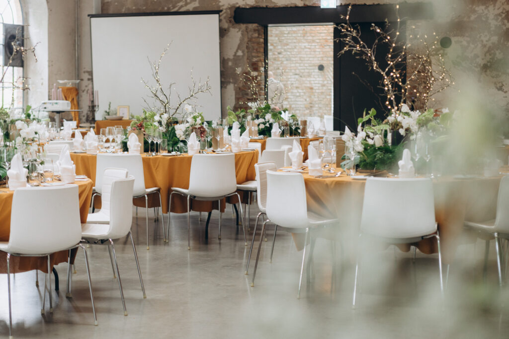 Festlich gedeckte Hochzeitstische mit weißen Orchideen, grünen Blättern und warmgelben Tischdecken im Essenssaal des Harbour Club Köln-Mülheim.